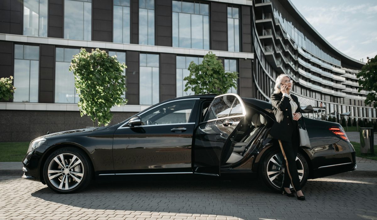 Confident businesswoman in suit using cellphone beside luxury car downtown.
