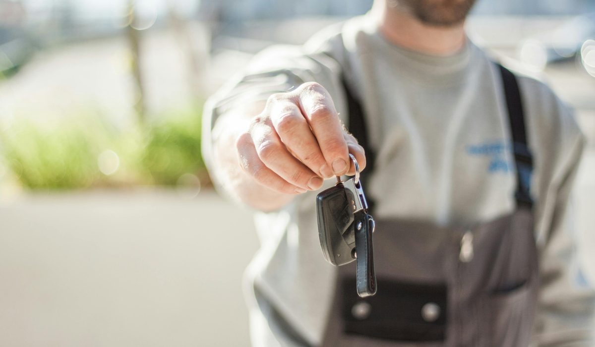 Hand holding a car key outdoors, blurred background, shallow focus.