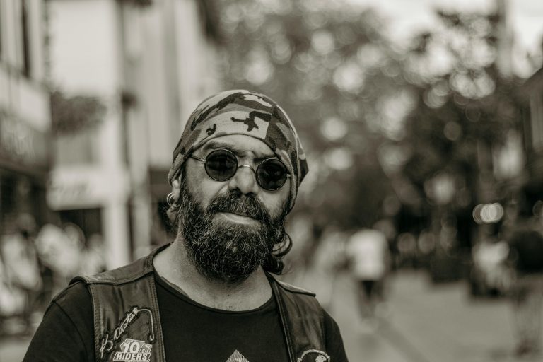 Black and white portrait of a bearded man with sunglasses and a bandana, urban background.